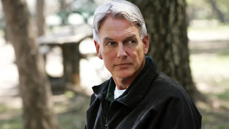 A medium shot photograph of actor Mark Harmon in character as Leroy Jethro Gibbs from NCIS, wearing his signature black jacket and green polo shirt, looking thoughtfully off-camera with a neutral expression.