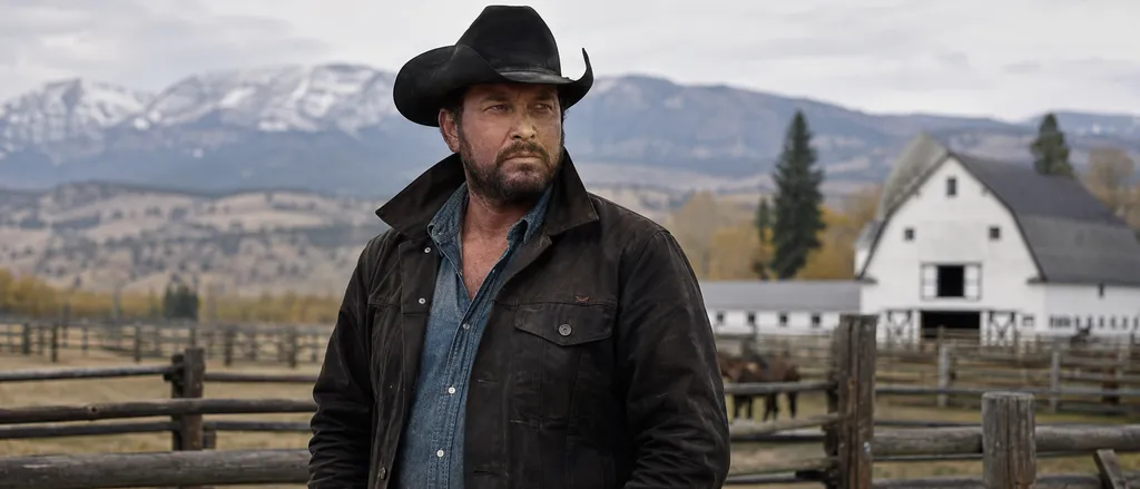 Rip Wheeler standing on the Yellowstone ranch with mountains and a barn behind him