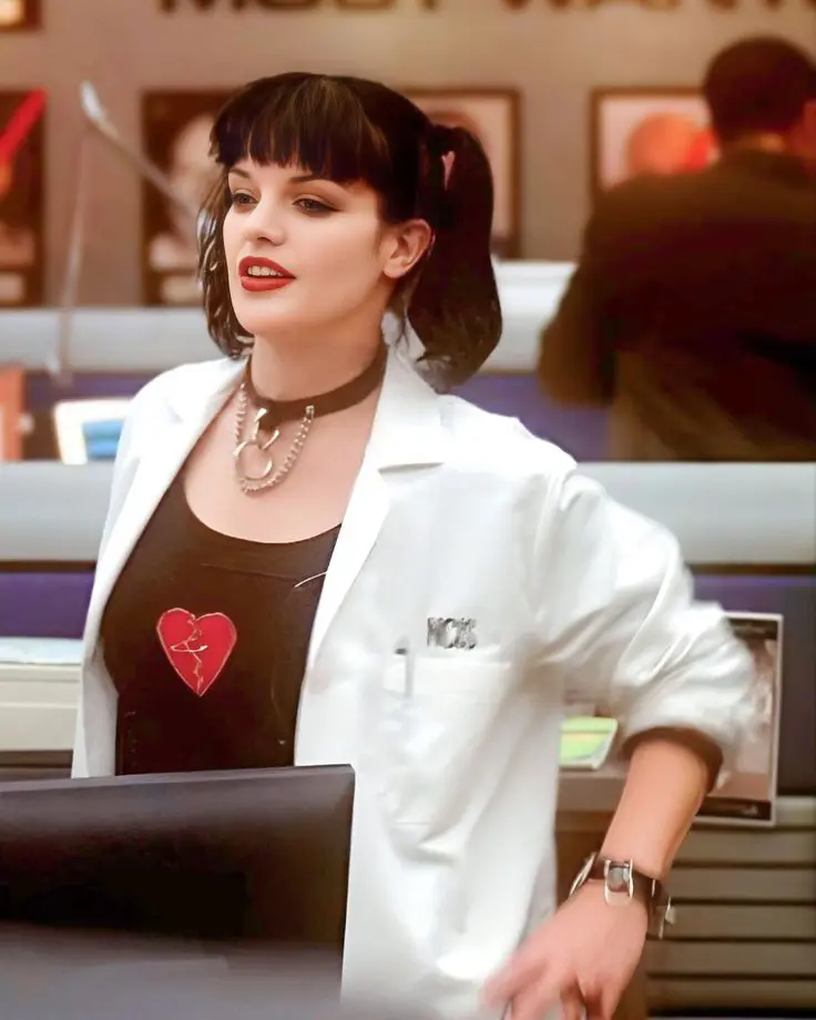 Pauley Perrette as Abby Sciuto wearing a white lab coat and pigtails in the NCIS forensic lab