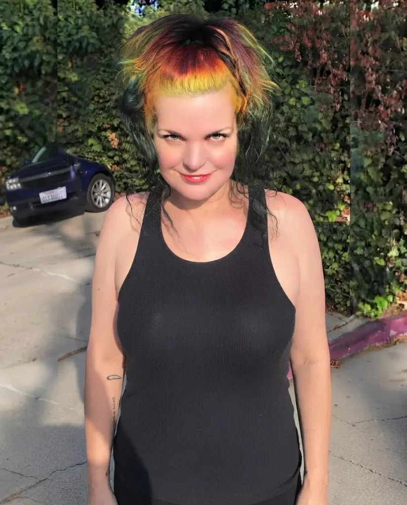 Pauley Perrette with rainbow-colored hair in a casual outdoor portrait