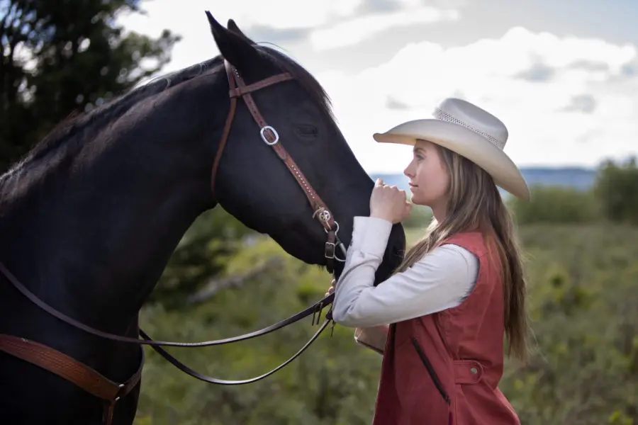Amber Marshall standing beside her horse on the ranch, reflecting her real-life connection with animals and her Heartland character, Amy Fleming.