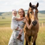 Amber Marshall standing beside a chestnut horse on her Alberta ranch at sunset.