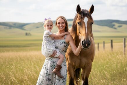 Amber Marshall standing beside a chestnut horse on her Alberta ranch at sunset.