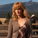 4k still of Kelly Reilly as Beth Dutton in a brown cardigan and plaid dress, standing on the Dutton Ranch with mountains in the background.