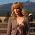 4k still of Kelly Reilly as Beth Dutton in a brown cardigan and plaid dress, standing on the Dutton Ranch with mountains in the background.