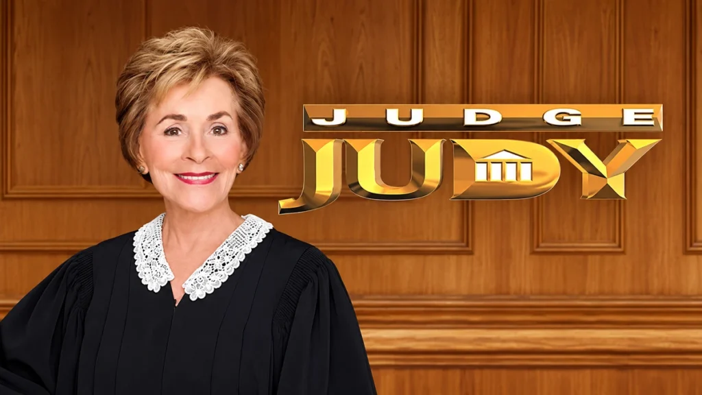 Judge Judy smiling in her courtroom robe beside the Judge Judy show logo against a wood-paneled courtroom background